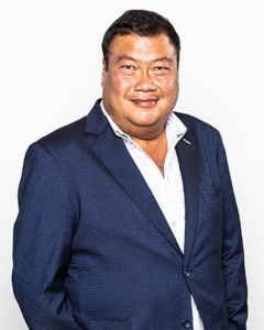 Jose Banzon wearing a navy suit and smiling at camera white background