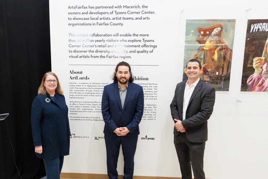Three people stand in front of a wall sign for the exhibition that reads "ArtsFairfax has partnered with Macerich, the owners and developers of Tysons Corner Center to showcase local artists, artist teams and arts organizations in Fairfax County."