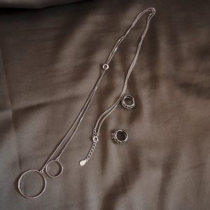 two rings and a necklace in silver tone lay on gray fabric