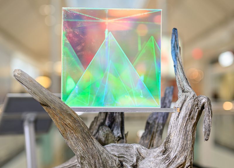 a transparent prismatic cube sits atop driftwood in this sculpture