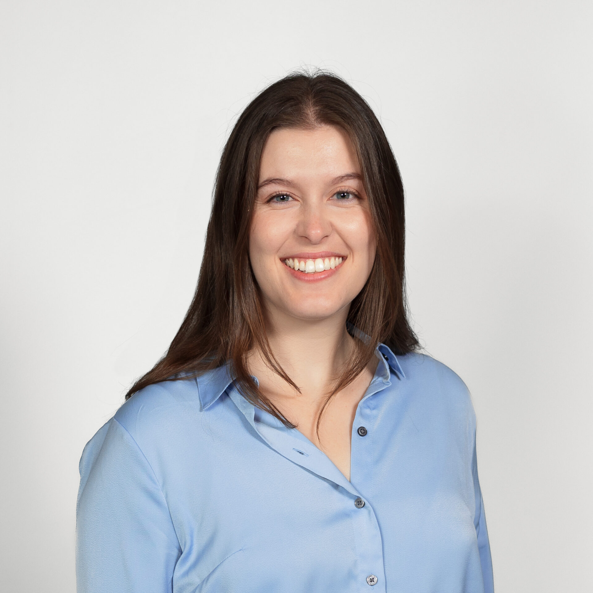 A smiling woman with light brown long hair wearing a light blue blouse