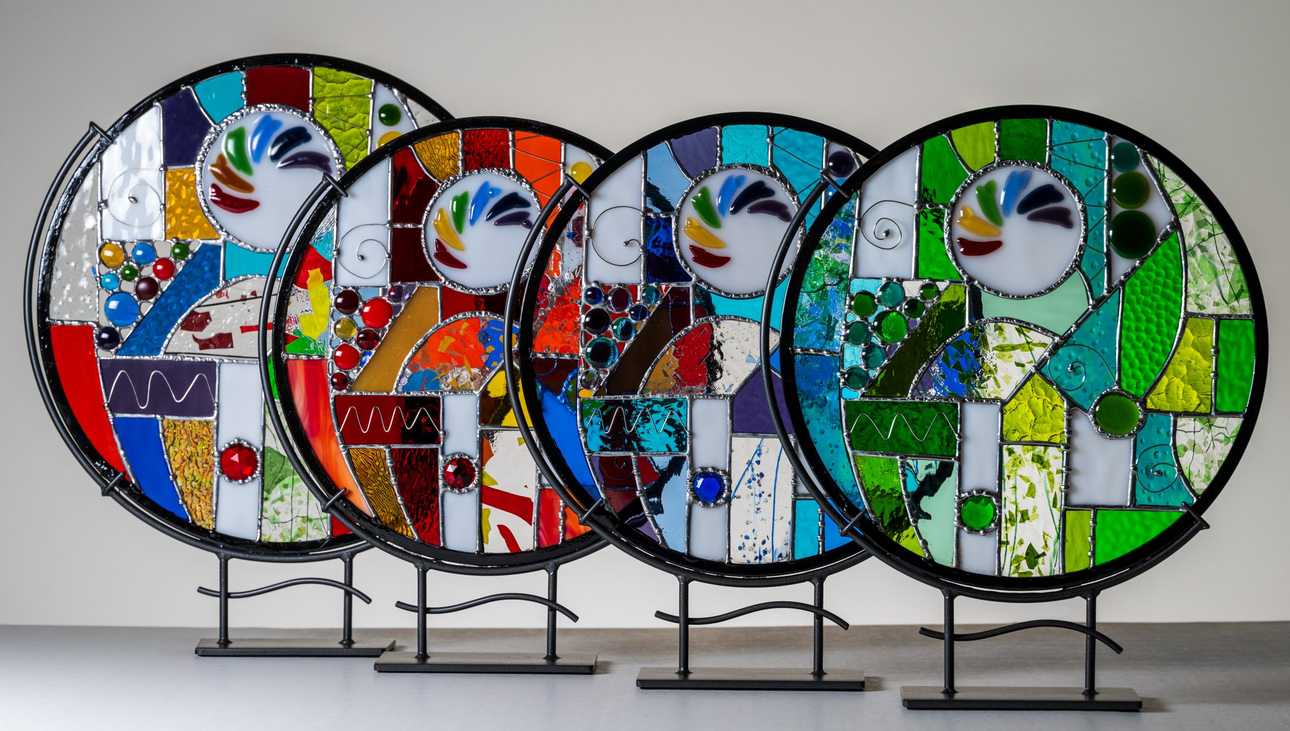 Four large works of circular stained glass stand on metal frames.