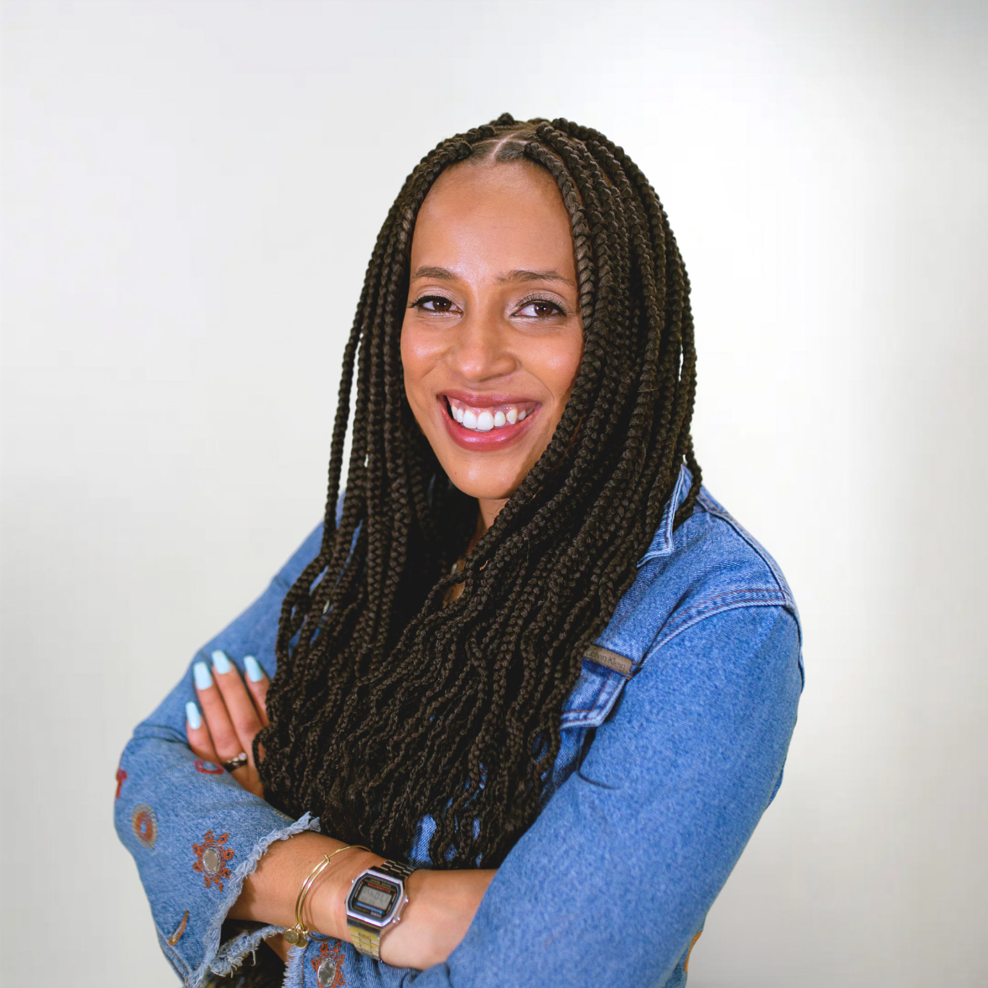 A woman with dark braided hair is wearing a jean shirt and smiles in a headshot photo.